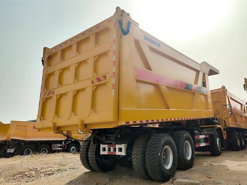 SHANTUI SK105 110-ton mining dump truck side profile on mine site, showing large cargo box and 10-wheel configuration.